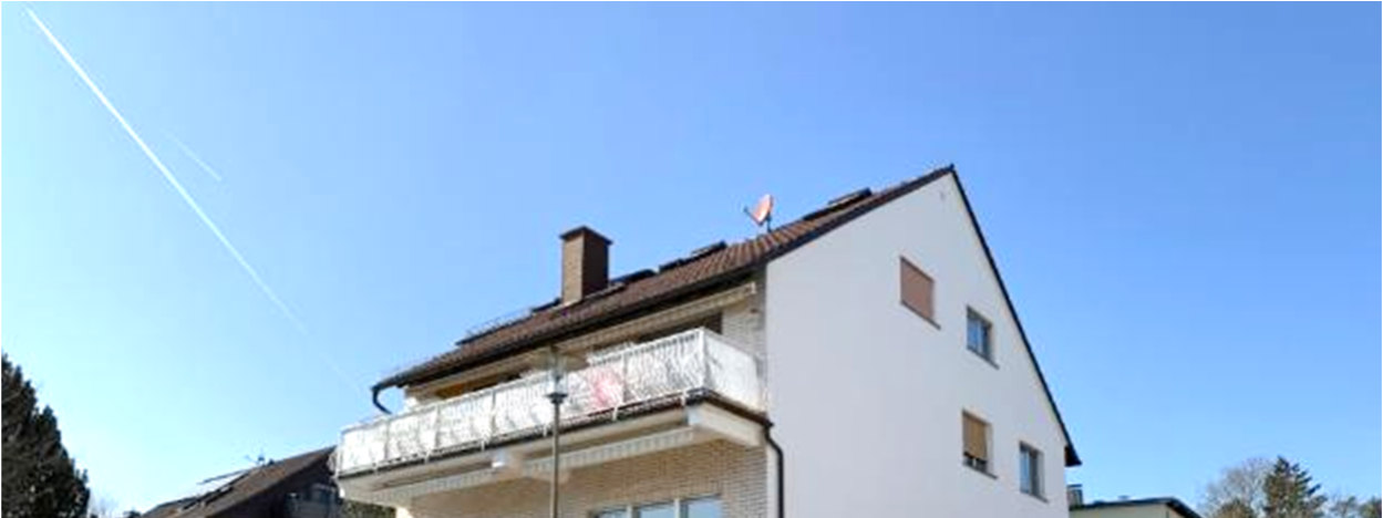 Seitenansicht eines zweistöckigen Wohnhauses mit Balkon, Dach und Schornstein unter klarem Himmel