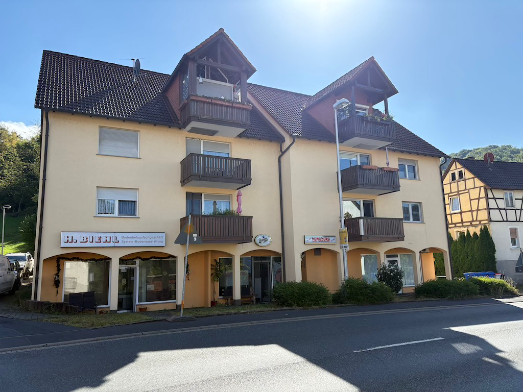 Gewerbeobjekt in Mömbris, Alzenauer Straße 4, gelb gestrichenes Gebäude mit Balkonen und Ladenfronten, sonniger Tag