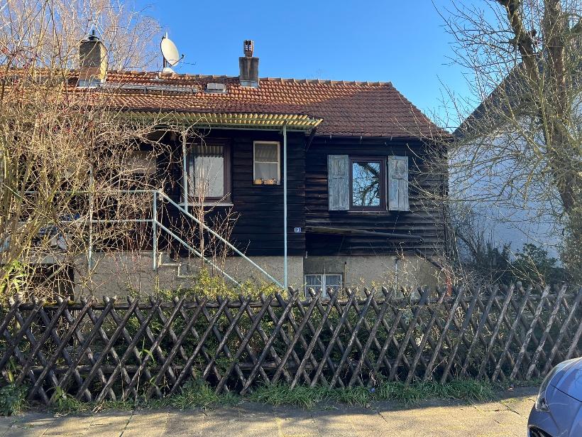 Vorderansicht eines Holzhauses mit rotem Ziegeldach, Fenstern mit Läden, Eingangstreppe und Holzzaun vorne. Lage: Bürgermeister-Beheim-Straße 3, 63165 Lämmerspiel