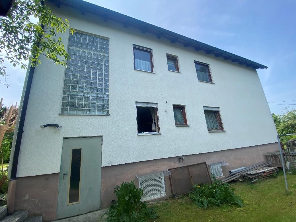 Seitenansicht eines zweistöckigen Wohnhauses mit Fenstern, einer Tür und Gartenfläche im Vordergrund