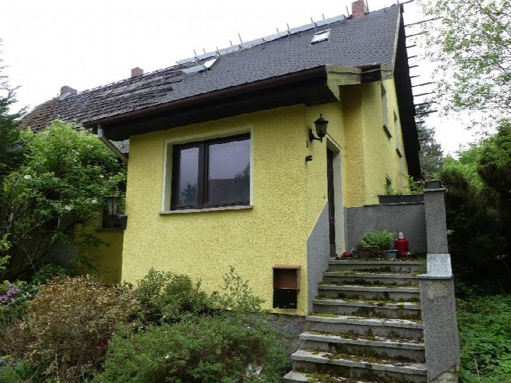 Eingangsbereich einer gelben Doppelhaushälfte mit Stufen, Fenster und Außenlampe; umgeben von Grünanlagen