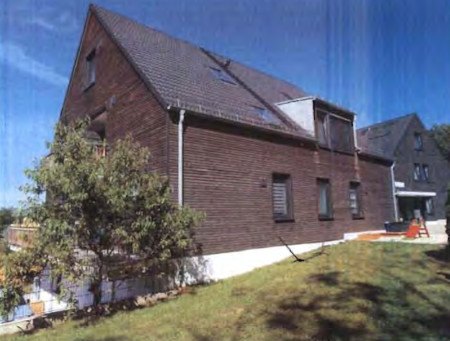 Seitenansicht eines Einfamilienhauses in Moosburg, Münchener Straße 88, mit dunkelbrauner Holzfassade, Satteldach und Dachfenstern. Grünfläche im Vordergrund