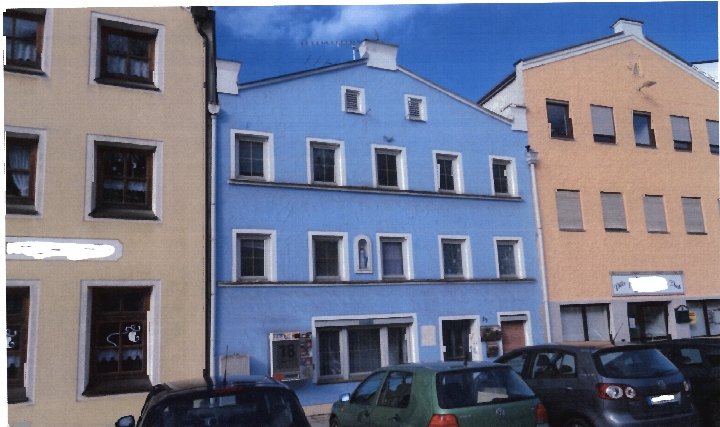 Fassade eines Wohn- und Geschäftshauses in Tann, Marktplatz 34, mit blauem Mittelteil und beigen Seitenflügeln, mehrere Fenster, geparkte Autos vorne