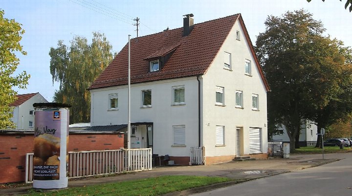 Zweistöckiges weißes Gebäude mit rotem Satteldach an der Adolf-Wolf-Straße 22 in Weißenhorn, 89264. Vorderansicht mit Einfahrt, Fenstern und angrenzender Mauer