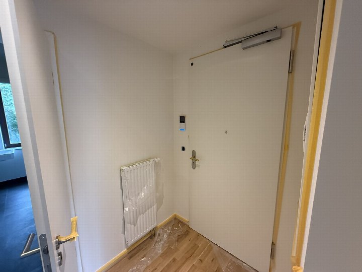 Eingangsbereich einer Gewerbeeinheit in Leipzig, Ferdinand-Lassalle-Str. 11, mit weißer Tür, Heizkörper und Holzboden, teilweise mit Schutzfolie abgedeckt