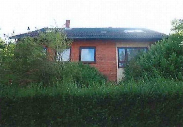 Seitenansicht eines Mehrfamilienhauses mit roten Ziegelwänden, dunklem Dach und Fenstern, teilweise von Büschen verdeckt, Heikendorfer Weg 74, 24149 Kiel