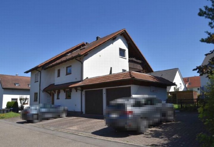Vorderansicht eines Mehrfamilienhauses in Bondorf, Wengertsteig 6, mit weißer Fassade, braunem Satteldach und integriertem Carport. Zwei geparkte Fahrzeuge vor dem Haus