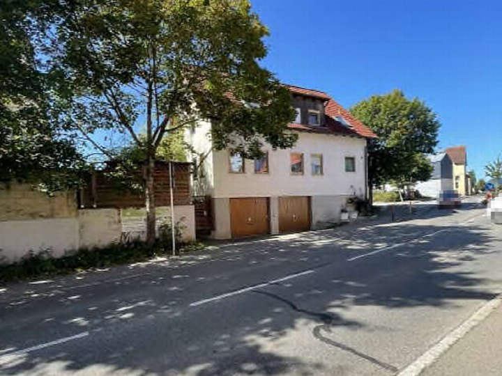 Seitenansicht eines zweistöckigen Gebäudes mit rotem Satteldach und Holztoren im Erdgeschoss an der Herrenberger Straße 43 in Ammerbuch, 72119. Bäume und Straße im Vordergrund