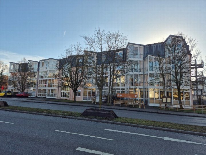 Fassade eines mehrstöckigen Gebäudes in Ansbach, Ludwig-Keller-Str. 40, mit Glasfassaden und Balkonen, umgeben von kahlen Bäumen und Straße