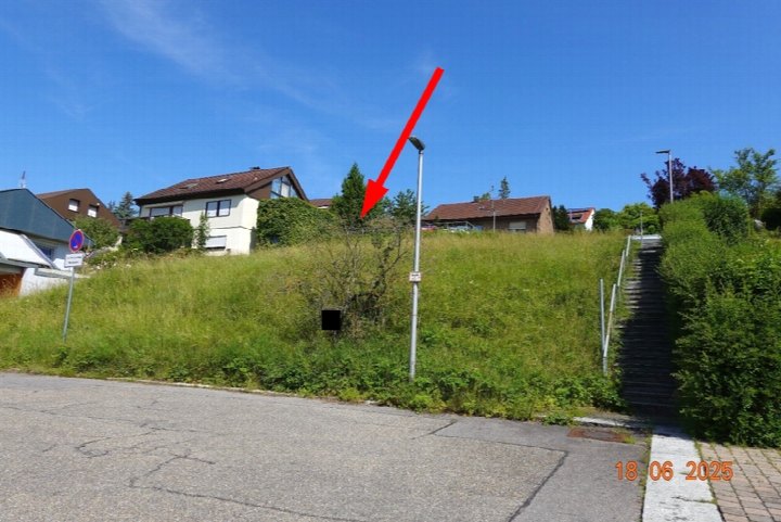 Unbebautes Grundstück in Weissach, Jakobsäcker, mit Grünfläche, Bäumen und einem Treppenaufgang; im Hintergrund Wohnhäuser unter blauem Himmel