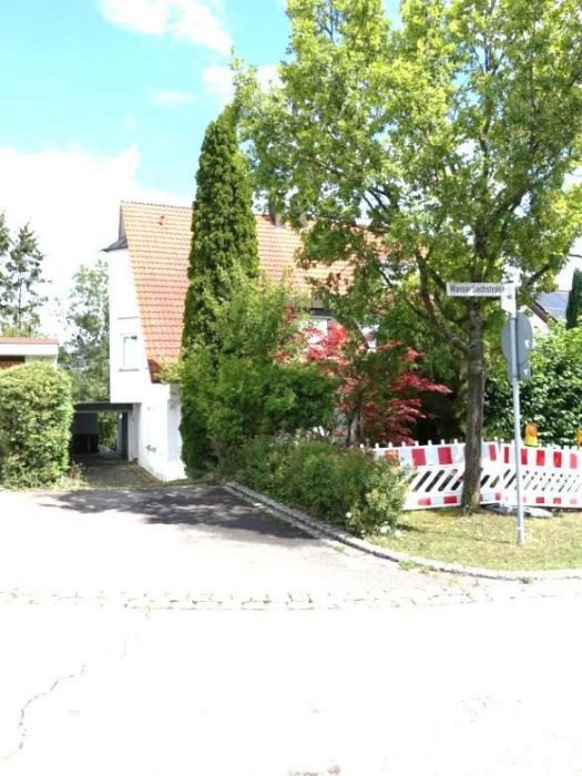 Vorderansicht einer Doppelhaushälfte in Leonberg, Wasserbachstraße 29, mit weißer Fassade, rotem Ziegeldach, Einfahrt und grüner Umgebung unter blauem Himmel