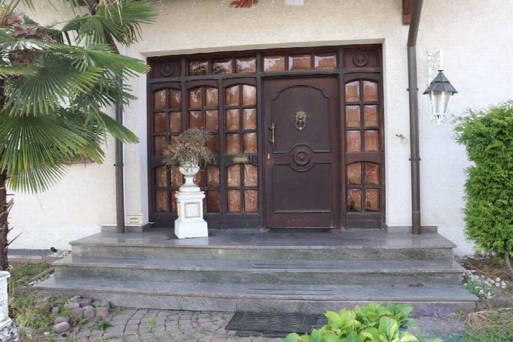 Eingangsbereich eines Einfamilienhauses mit dunkler Holztür, Glasfenstern, Stufen und einem weißen Blumentopf. Links Palme, rechts Hecke. Adresse: Am Lohbachhang 15, Dortmund