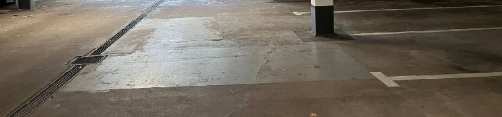 Betonboden einer Tiefgarage mit Parkplatzmarkierungen und Abflussgitter