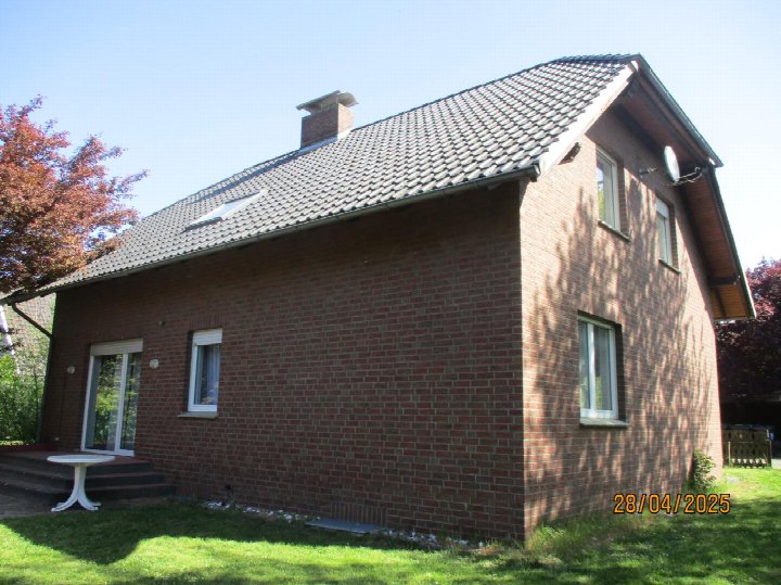Seitenansicht eines Einfamilienhauses aus roten Ziegeln mit Satteldach, Fenstern, Schornstein und angrenzendem Rasen in Raddestorf