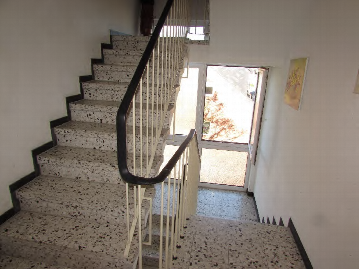 Treppenhaus mit Terrazzotreppe, Metallgeländer und Tür zum Außenbereich