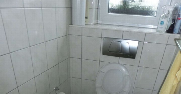 Badezimmer mit weißen Fliesen, Wandspülung und Fenster, Toilette mit geschlossenem Deckel