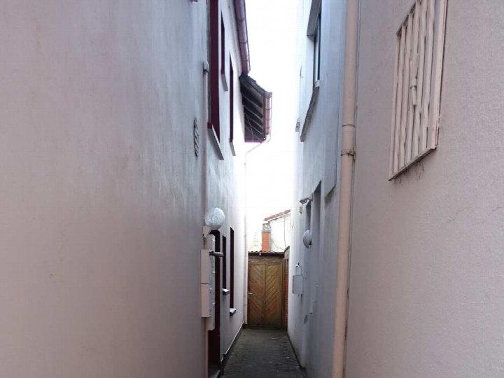 Schmale Gasse zwischen zwei Gebäuden mit sichtbaren Wänden, Fenstern und einem Tor am Ende, Ansicht der Seitenfassade des Wohn-/Geschäftshauses in Edewecht