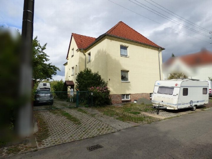 Seitenansicht eines zweistöckigen Wohnhauses mit rotem Ziegeldach und cremefarbener Fassade in Neukieritzsch, Neue Str. 7, mit geparktem Wohnwagen vor dem Grundstück