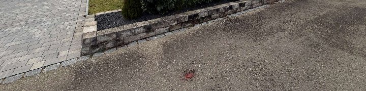 Pflasterfläche neben einer Steinmauer mit einem roten Abdeckelement auf dem Boden, Teil der Garage oder des Stellplatzes in Wilburgstetten