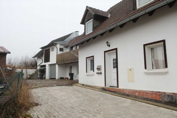 Einfamilienhaus mit weißer Fassade und braunen Fensterrahmen, Eingangstür mit Briefkasten und Laterne, gepflasterter Vorplatz
