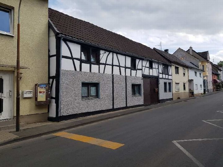 Seitenansicht eines Mehrfamilienhauses mit Fachwerk- und Putzfassade an der Hauptstraße in Alfter, mit angrenzenden Gebäuden und Straße im Vordergrund
