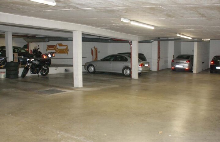 Untergeschoss-Parkgarage mit mehreren geparkten Fahrzeugen und Motorrädern, Betonpfeilern und Leuchtstoffröhrenbeleuchtung