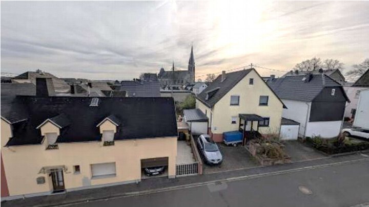 Seitenansicht eines Wohnhauses mit dunklem Dach, gelber Fassade, Garage und angrenzenden Häusern in einer Wohnstraße