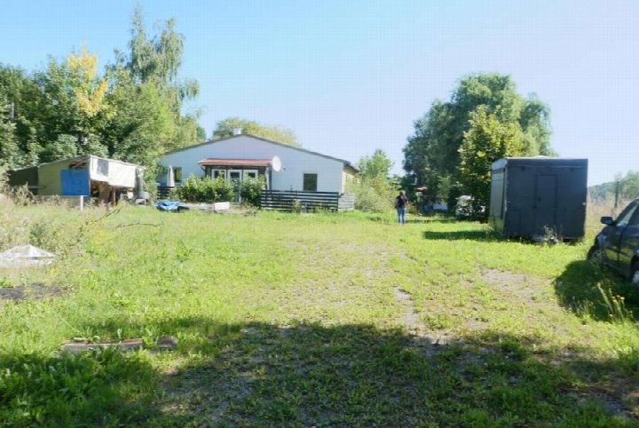 Grüner Außenbereich mit Gras, Bäumen und einem weißen Gebäude im Hintergrund, Teil des Grundstücks Lohmühlenweg 22 in Stadtilm