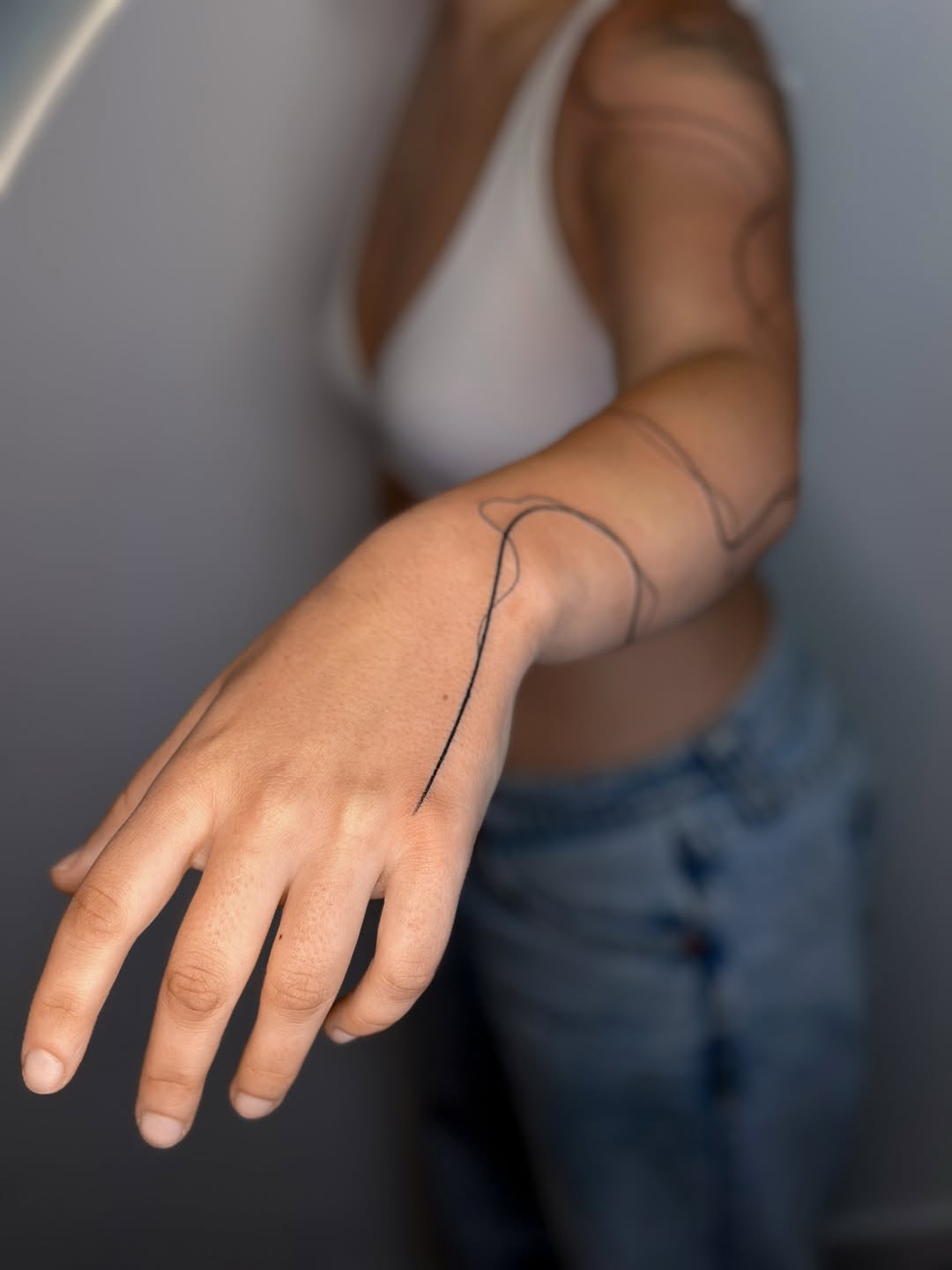 Minimalist single-line forearm design with flowing abstract curve.