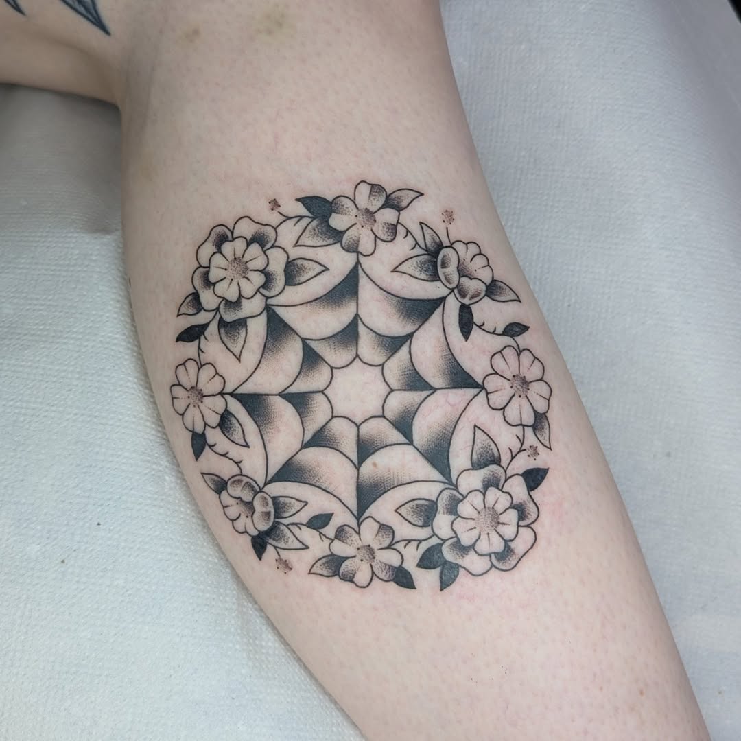 Circular blackwork spider-web framed by delicate floral accents