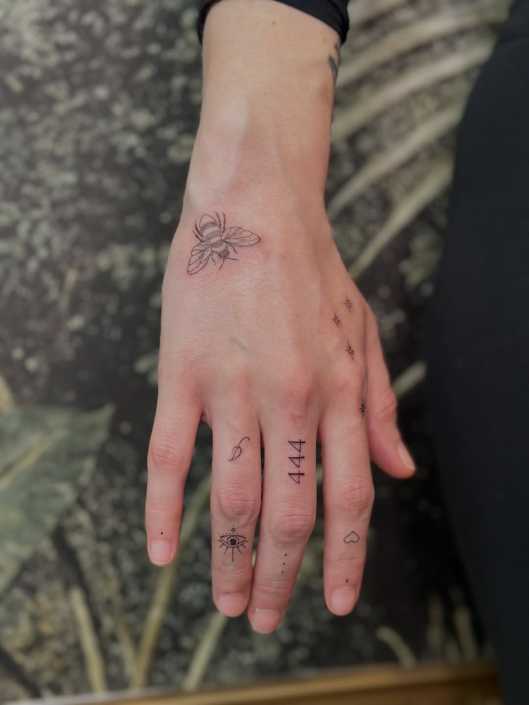 Delicate linework hand tattoos: bee, stars, eye.