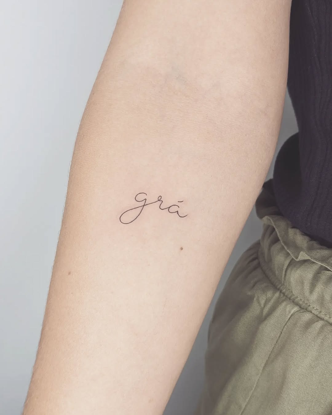 Delicate Gaelic script grá on the forearm.