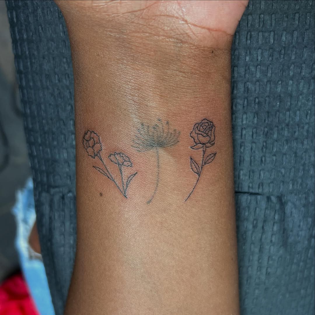 Delicate fine-line trio of garden flowers on forearm.