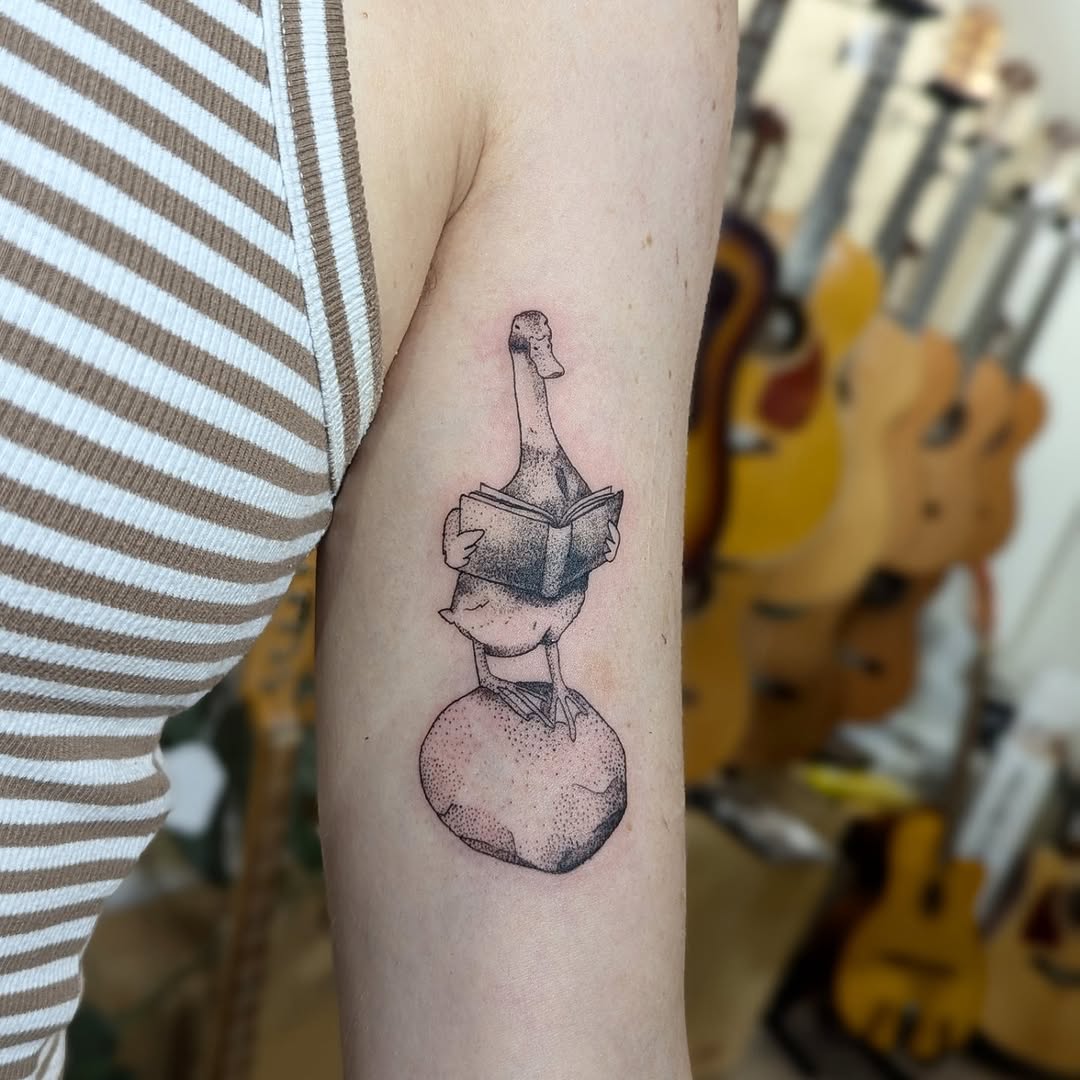 Whimsical fine-line goose reading a book tattoo