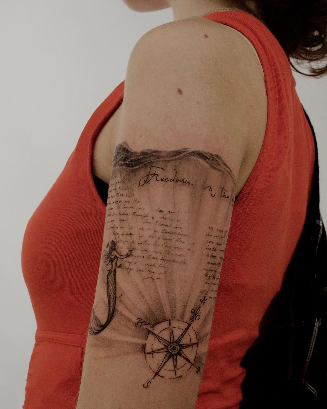 Delicate linework mermaid, compass, and cursive script tattoo