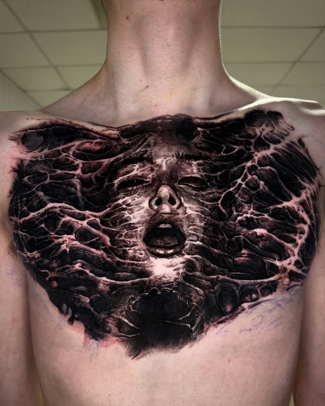 Dense blackwork chest piece with eerie organic-face motif