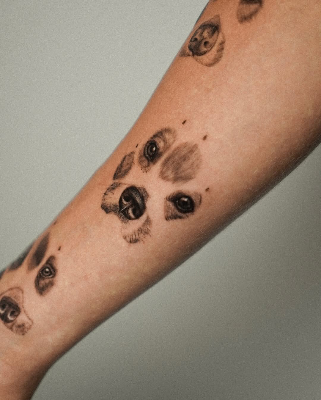 Delicate black-and-gray dog-face portraits along forearm.