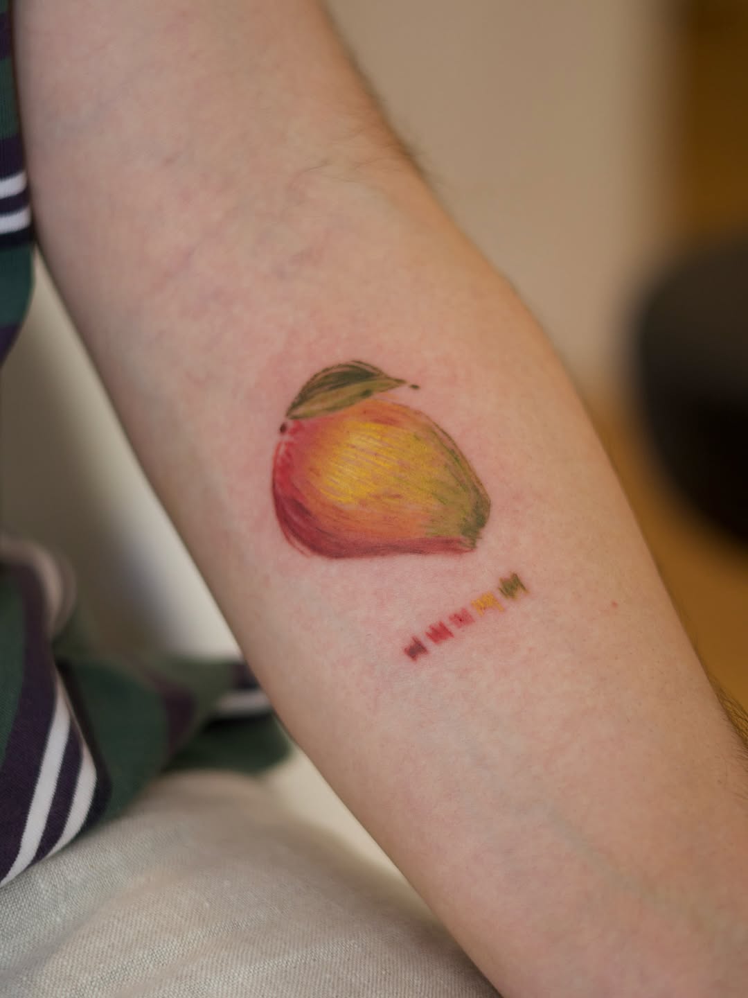 Vibrant watercolor mango on forearm, playful and bright.