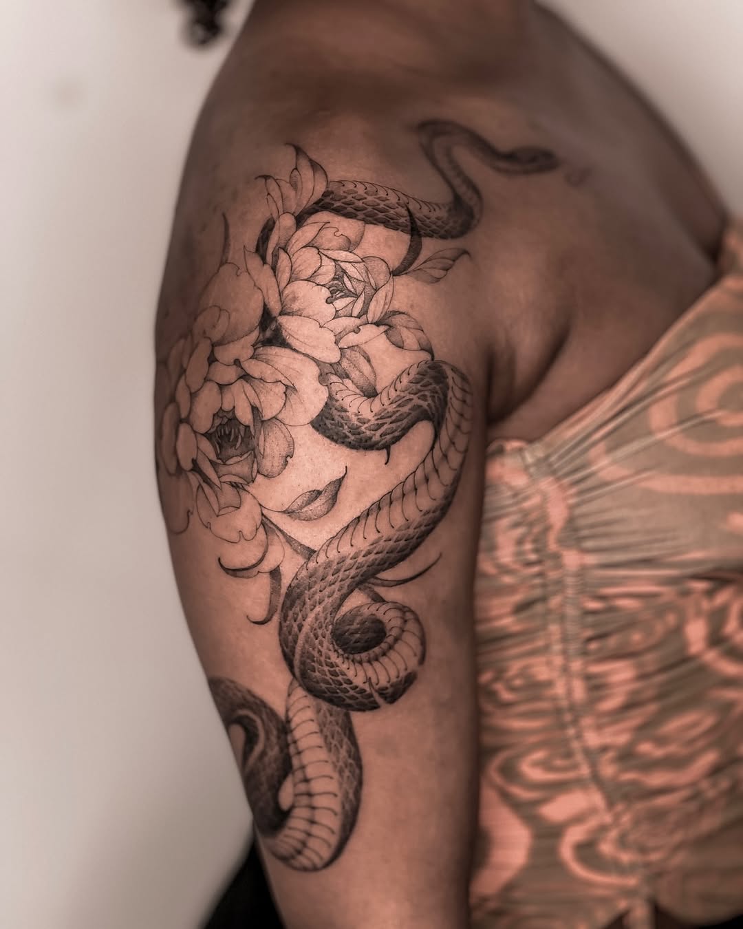 Bold snake winds through lush peony bouquet on arm