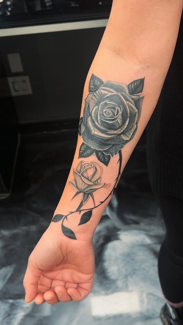 Bold grayscale rose on forearm with curling vines.