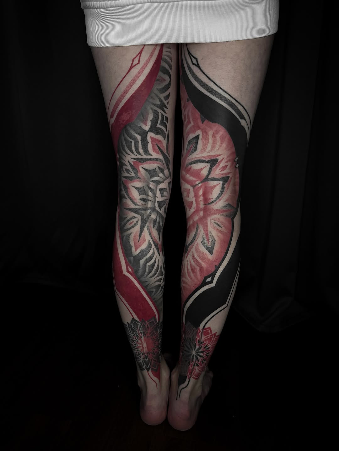 Bold geometric blackwork leg sleeves with crimson accents.