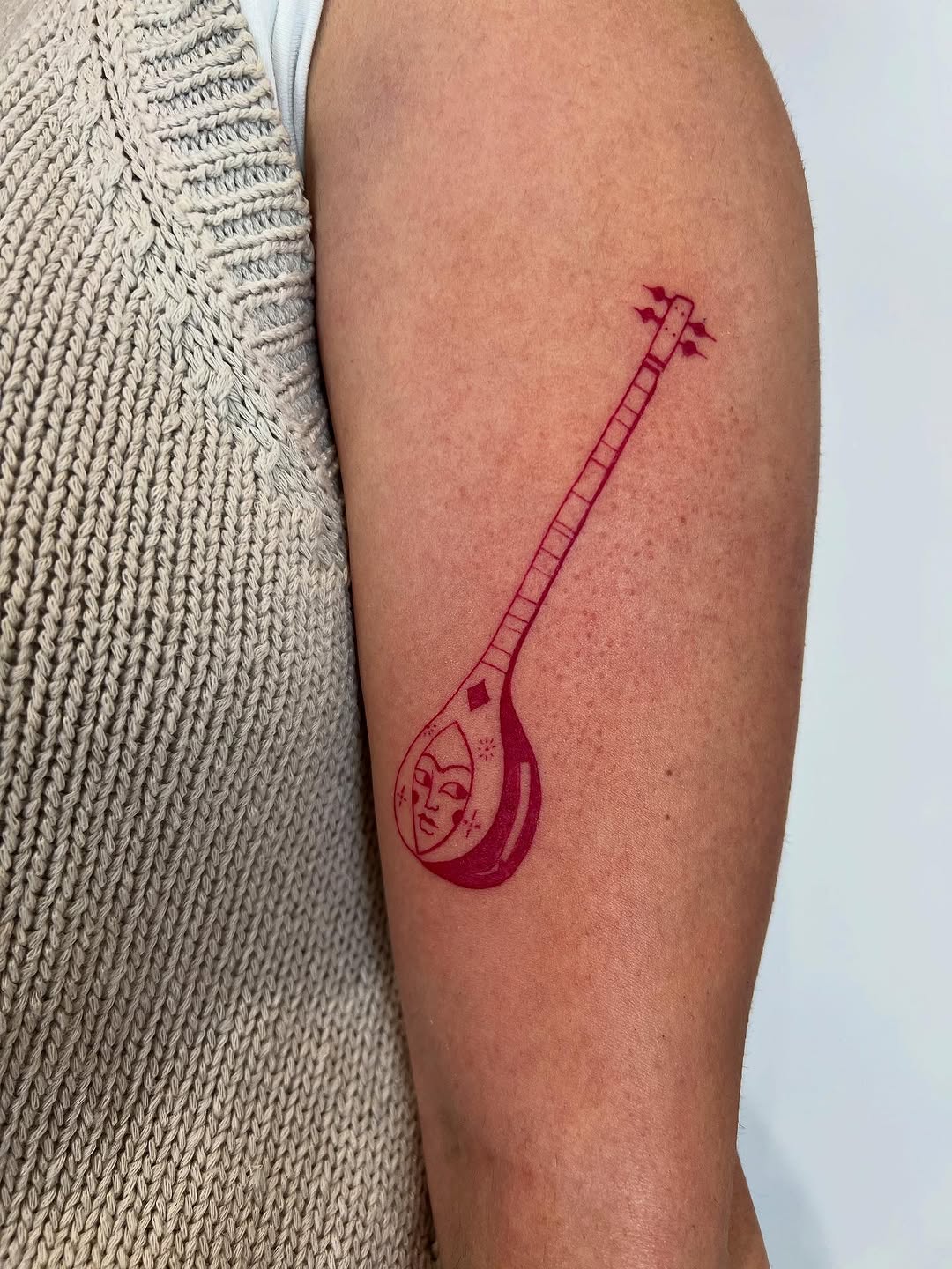 Red linework setar-inspired tattoo with moon-face detail