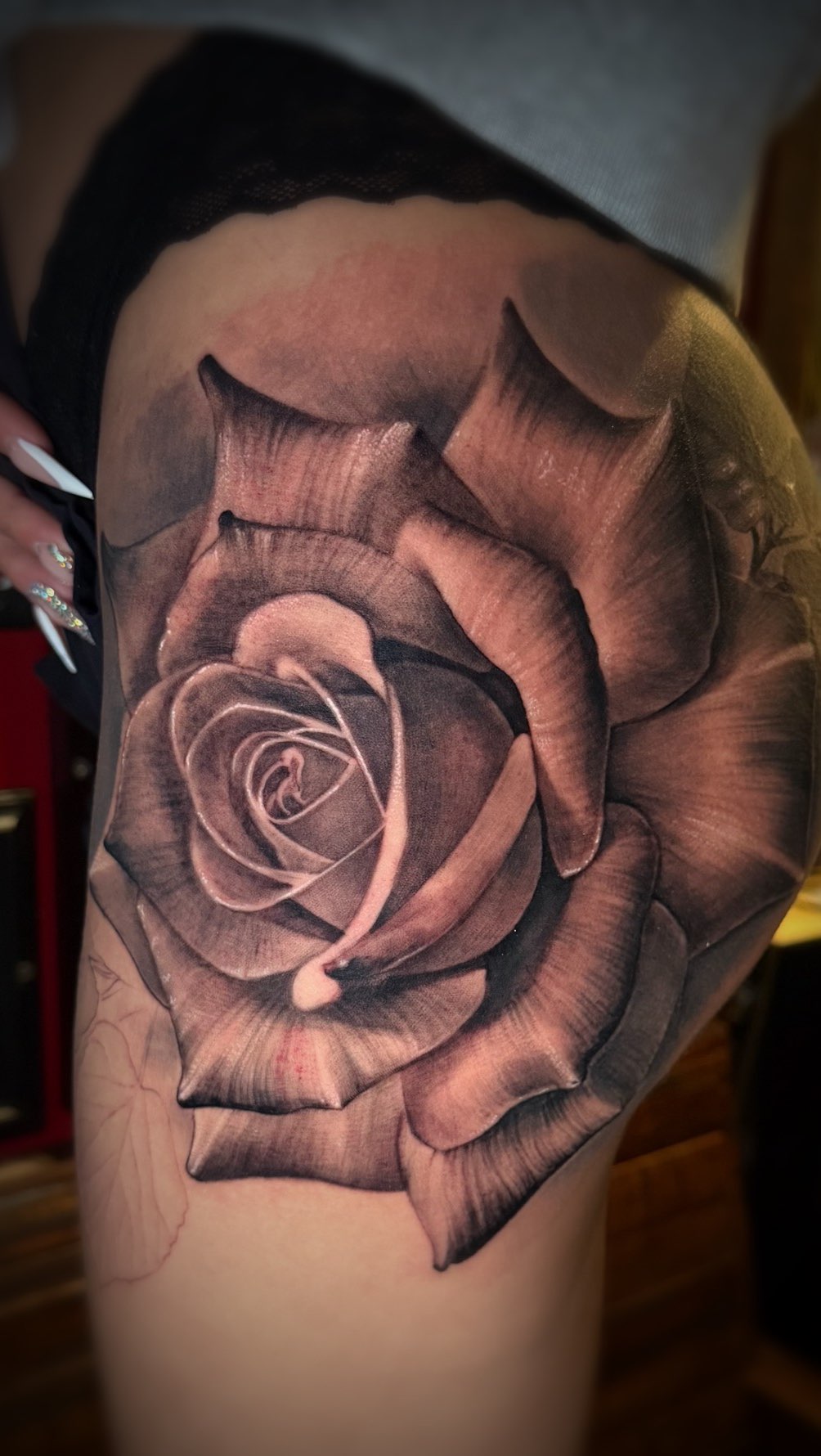Hyper-detailed black-and-gray rose, lifelike shading on outer thigh