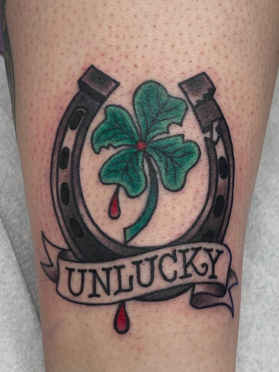 Bold traditional horseshoe with green clover, UNLUCKY banner