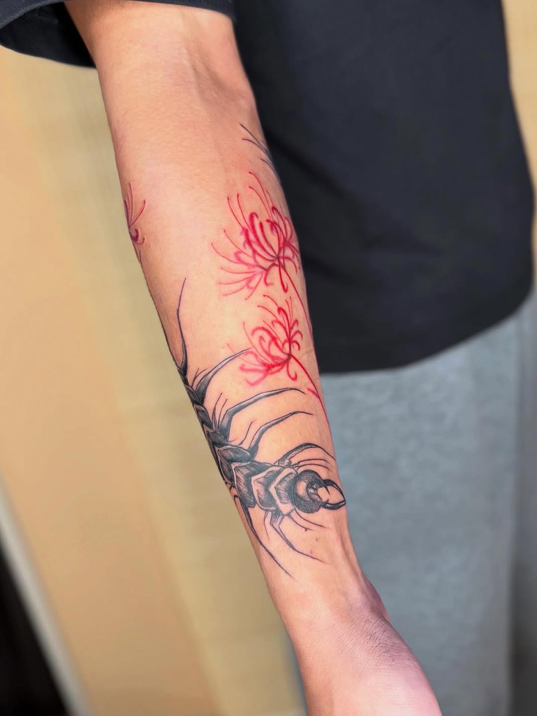 Intricate black floral vine with red-outline blossoms wrapping forearm.