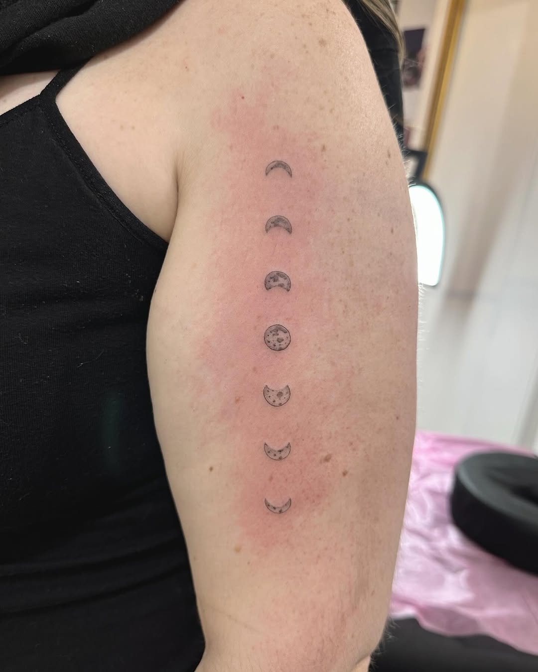 Delicate fine-line lunar phases tattoo along forearm.