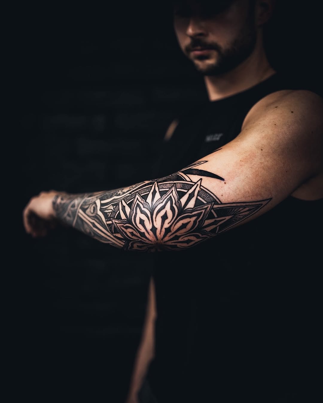 Bold geometric floral mandala forearm tattoo in blackwork.