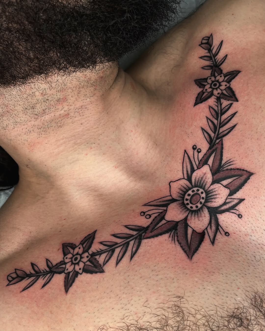 Bold black floral vine wrapping collarbone with stylized petals