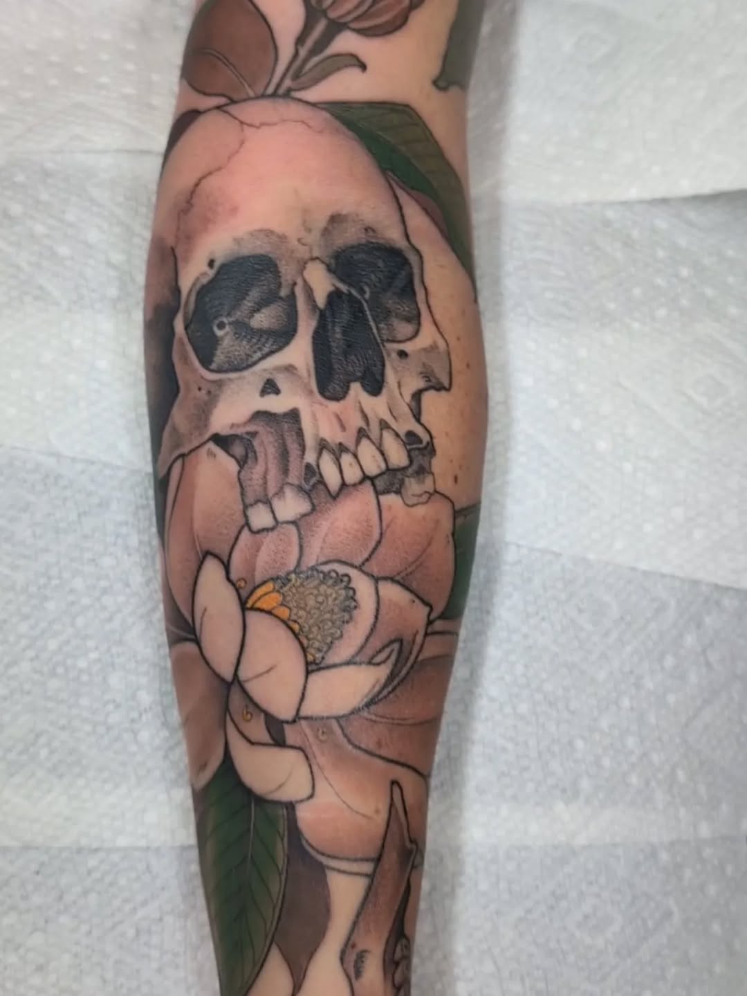 Bold skull entwined with magnolia blossoms; pink petals.