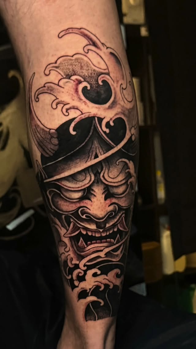 Bold black-and-gray oni mask carved through curling waves